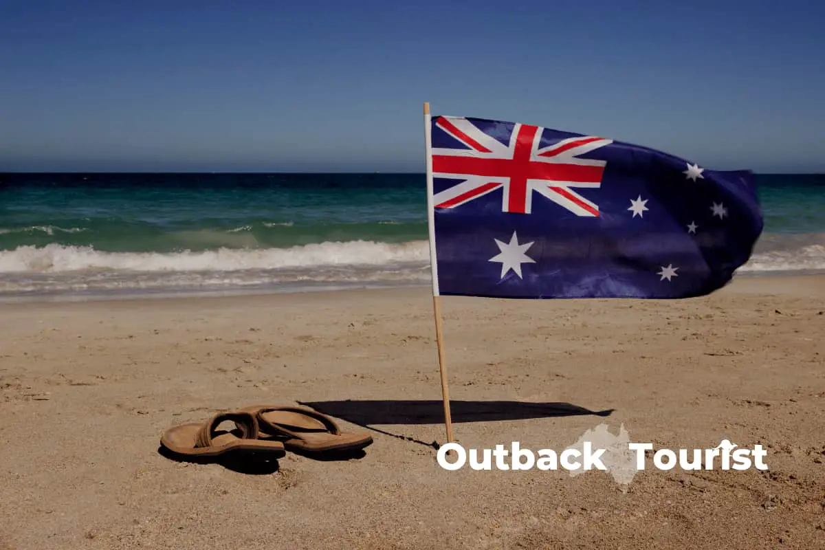 Australian flag buried in the beach next to flip flops and a nice wave in the background
